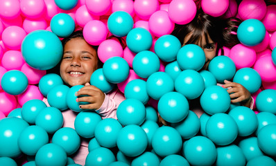 two little girls smiling and playing at blue and pink ball pool