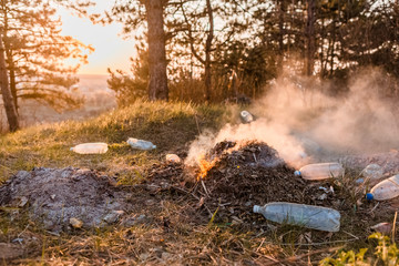 A heap of burning leaves next to a some plastic bottles in the forest.