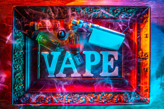 The vaping concept. White letters of the Latin alphabet and accessories for Smoking electronic cigarettes. Vaping devices in a carved frame. A picture of Smoking gadgets. E-cigarette smoke.