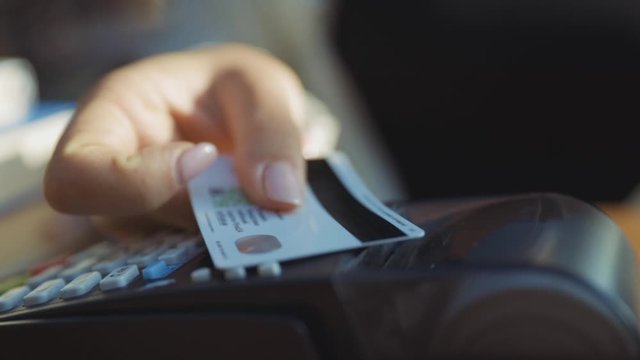Close-up of woman rotating credit card in hands applying on pos reader for checkout and wireless money transaction. Credit card payment. Outdoor view.