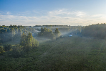 Fog floats over the forest and a field and a star-shaped tent