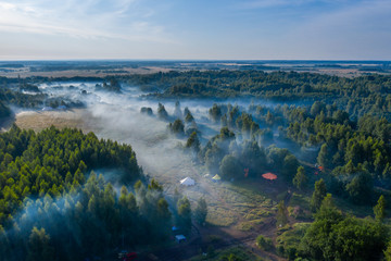 Fog floats over the forest and a field and a star-shaped tent