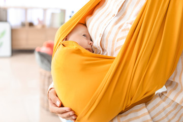 Young mother with little baby in sling at home, closeup