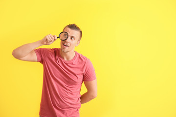 Young man with magnifying glass on color background