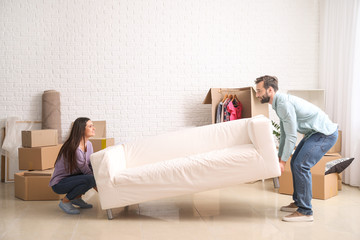 Young couple carrying sofa after moving into new house