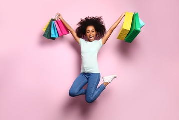 Portrait of jumping African-American woman with shopping bags on color background
