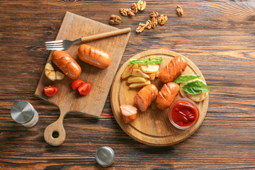 Tasty grilled sausages with sauce and potatoes on wooden table