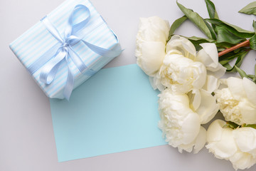 Gift box, blank card and beautiful flowers on light background