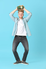 Happy young man with gift box on color background