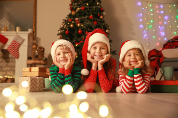 Fototapeta na wymiar Cute little children in Santa Claus hats lying on floor on Christmas eve at home
