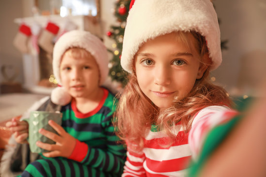 Cute little children in Santa Claus hats taking selfie at home