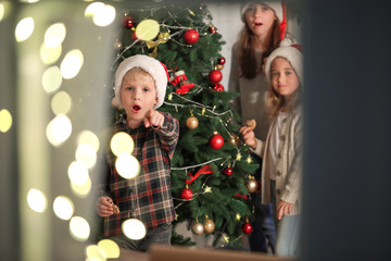 Surprised little children looking through window on Christmas eve at home