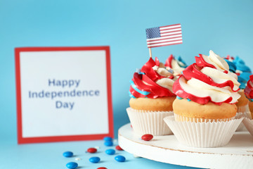 Tasty patriotic cupcakes and card with text HAPPY INDEPENDENCE DAY on color background