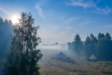 Morning fog evaporates from the field on which stands a star-shaped tent