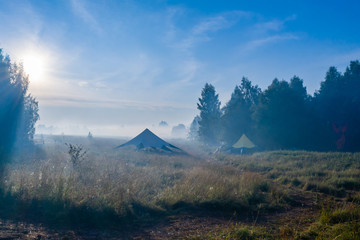 Morning fog evaporates from the field on which stands a star-shaped tent