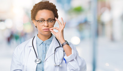 Young african american doctor woman wearing medical coat over isolated background mouth and lips shut as zip with fingers. Secret and silent, taboo talking