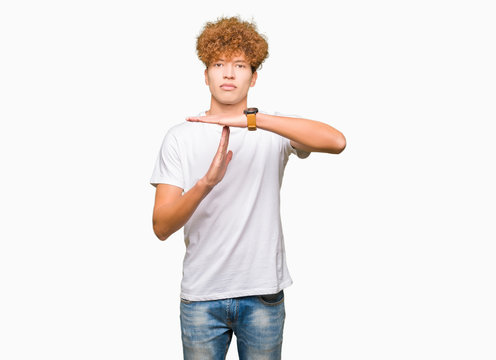 Young handsome man with afro hair wearing casual white t-shirt Doing time out gesture with hands, frustrated and serious face