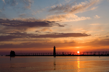 Fototapeta na wymiar The sun makes a perfect ball of light as it sets over Lake Michigan behind the Grand Haven Pierhead Light, Grand Haven, MI