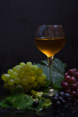grape brush and leaves and wine glass on black background selective focus