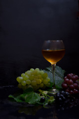 grape brush and leaves and wine glass on black background selective focus