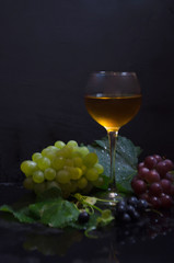 grape brush and leaves and wine glass on black background selective focus
