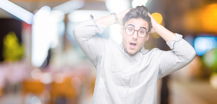 Young handsome man wearing glasses over isolated background Crazy and scared with hands on head, afraid and surprised of shock with open mouth