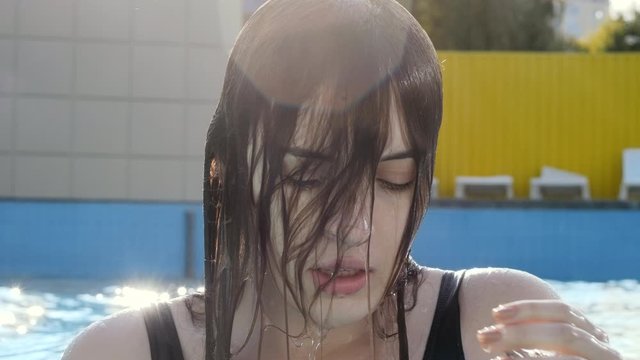 A young woman emerges from the water with a sunny sunset. Summer pool. Close-up. Portrait of a young girl.