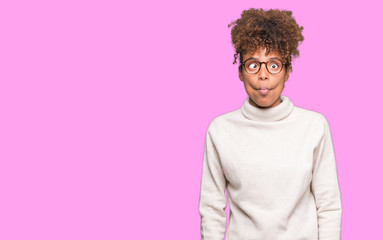 Fototapeta na wymiar Beautiful young african american woman wearing glasses over isolated background making fish face with lips, crazy and comical gesture. Funny expression.