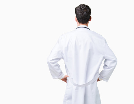 Young doctor man wearing hospital coat over isolated background standing backwards looking away with arms on body