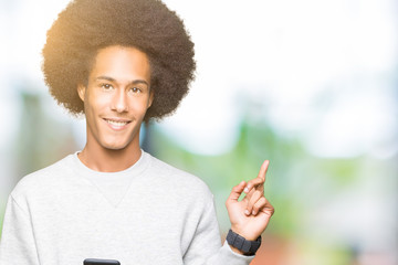 Young african american man with afro hair using a smartphone very happy pointing with hand and finger to the side