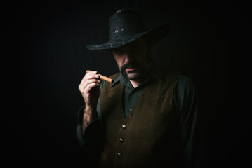 Portrait of a cowboy holding a cigar, with a dark background.