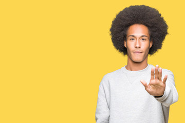 Young african american man with afro hair wearing sporty sweatshirt doing stop sing with palm of the hand. Warning expression with negative and serious gesture on the face.