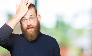 Obraz premium Young blond man wearing glasses and turtleneck sweater surprised with hand on head for mistake, remember error. Forgot, bad memory concept.