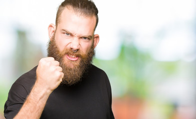 Fototapeta premium Young blond man wearing casual t-shirt angry and mad raising fist frustrated and furious while shouting with anger. Rage and aggressive concept.