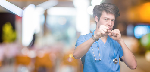 Young doctor wearing medical uniform over isolated background Punching fist to fight, aggressive...