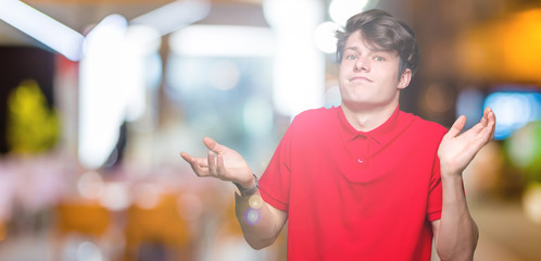 Young handsome man wearing red t-shirt over isolated background clueless and confused expression...
