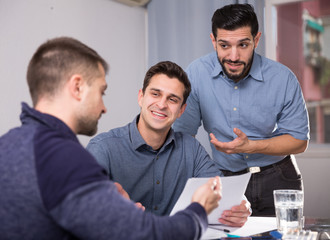 Two positive men helping friend with documents at table