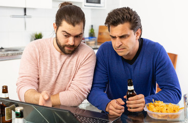 Friendly male meeting over beer at home, men looking at laptop and discussing