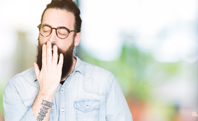 Fototapeta na wymiar Young hipster man with long hair and beard wearing glasses bored yawning tired covering mouth with hand. Restless and sleepiness.