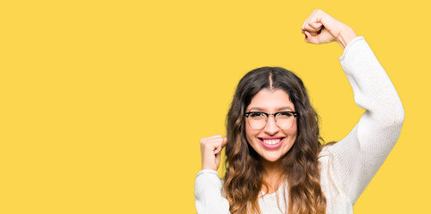 Young beautiful woman wearing glasses very happy and excited doing winner gesture with arms raised, smiling and screaming for success. Celebration concept.