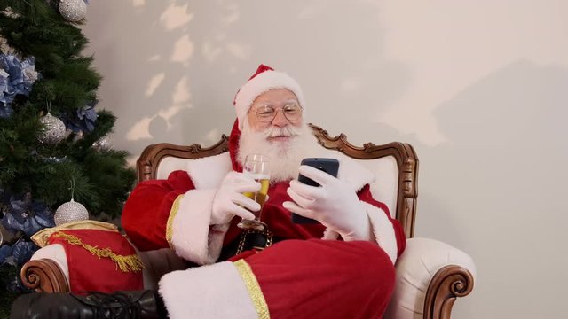 Santa Claus drinking a glass of beer while using his cellphone. Rest time. Alcoholic drink at the holidays. Drink with moderation. Craft beer. Merry Christmas. Cinematic 4K.