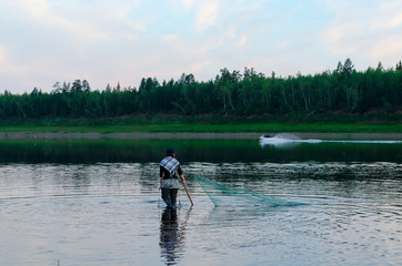 Fototapeta na wymiar Two men-Yakuts and graceful girl in a Shawl in the background of a boat go in wading boots through the wild North river Vilyui, which are traditionally caught by the dragnet of the local fish tugun.