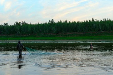 Two men Yakuts go in wading boots with fish net on the wildlife in the river Vilyuy in a forest...