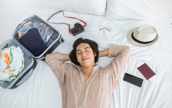 Portrait Of Young Asian Man Traveler Prepare Suitcase For Holiday Vacation. Top Overhead View Of Couple Of Tourists Lying On Bed In Hotel Room. Asian Backpacker Travel Lifestyle Concept Banner