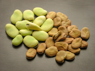 Dried and fresh fava beans on wooden table with black background