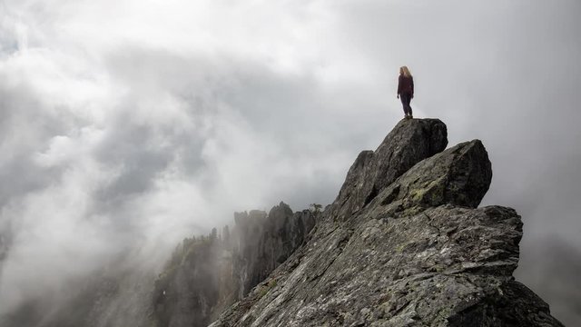 Cinemagraph of an Adventurous Girl on top of a rugged rocky mountain during a cloudy summer morning. Taken on Crown Mountain, North Vancouver, BC, Canada. Still Image Continuous Animation