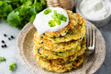 Zucchini fritters or pancakes stack with sour cream on top. Healthy vegetable patties