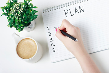 Female hand writes a plan in a notebook, goal setting concept