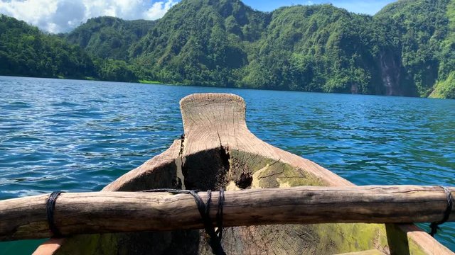An 8 seconds footage of a single wooden boat roaring into the lake with green forest in the background.