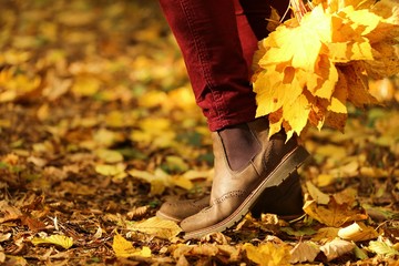 Autumn time.  legs in brown suede boots on a blurred yellow leaves background. Fashionable autumn shoes